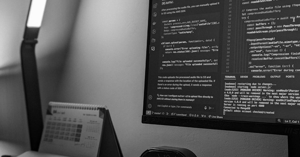 Black and white photo of a workspace featuring a monitor with coding screen, laptop, and desk lamp.
